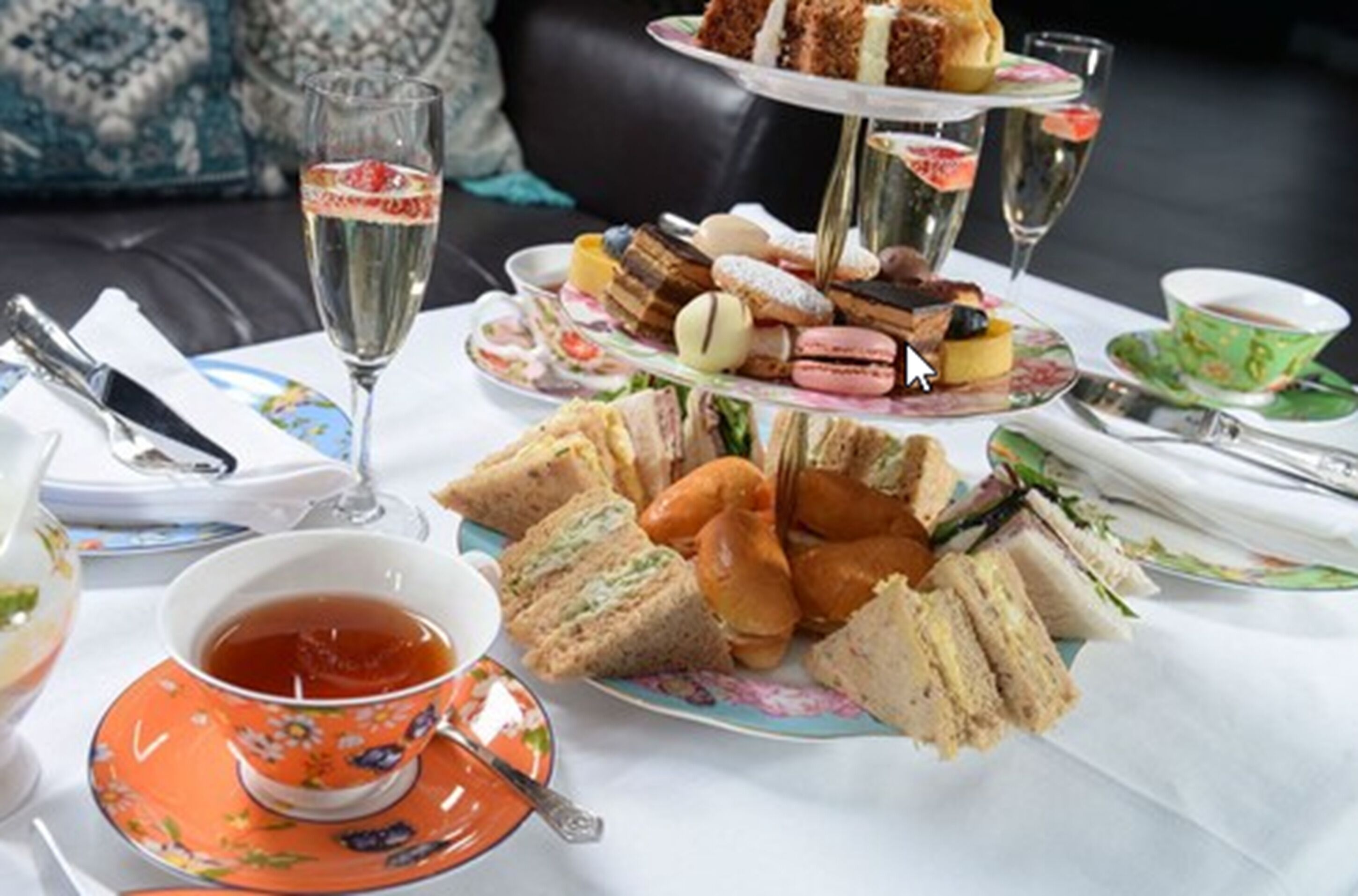 A three-tiered dessert stand with various pastries and sandwiches, a glass of champagne, and a cup of tea on a table.