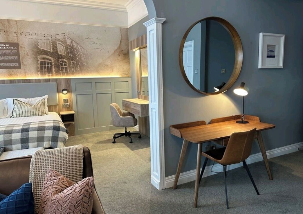 A bedroom with a bed, desk, chair, and a large mirror.