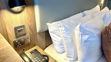 A hotel room with a wooden headboard, a bedside telephone, a wall-mounted light, and a bed with white pillows.