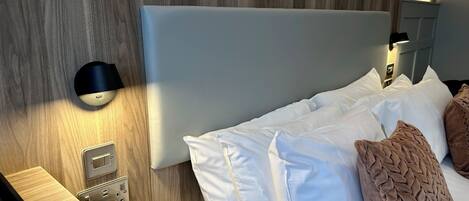Una habitación de hotel con cabecera de madera, teléfono en la mesita de noche y lámpara de pared.