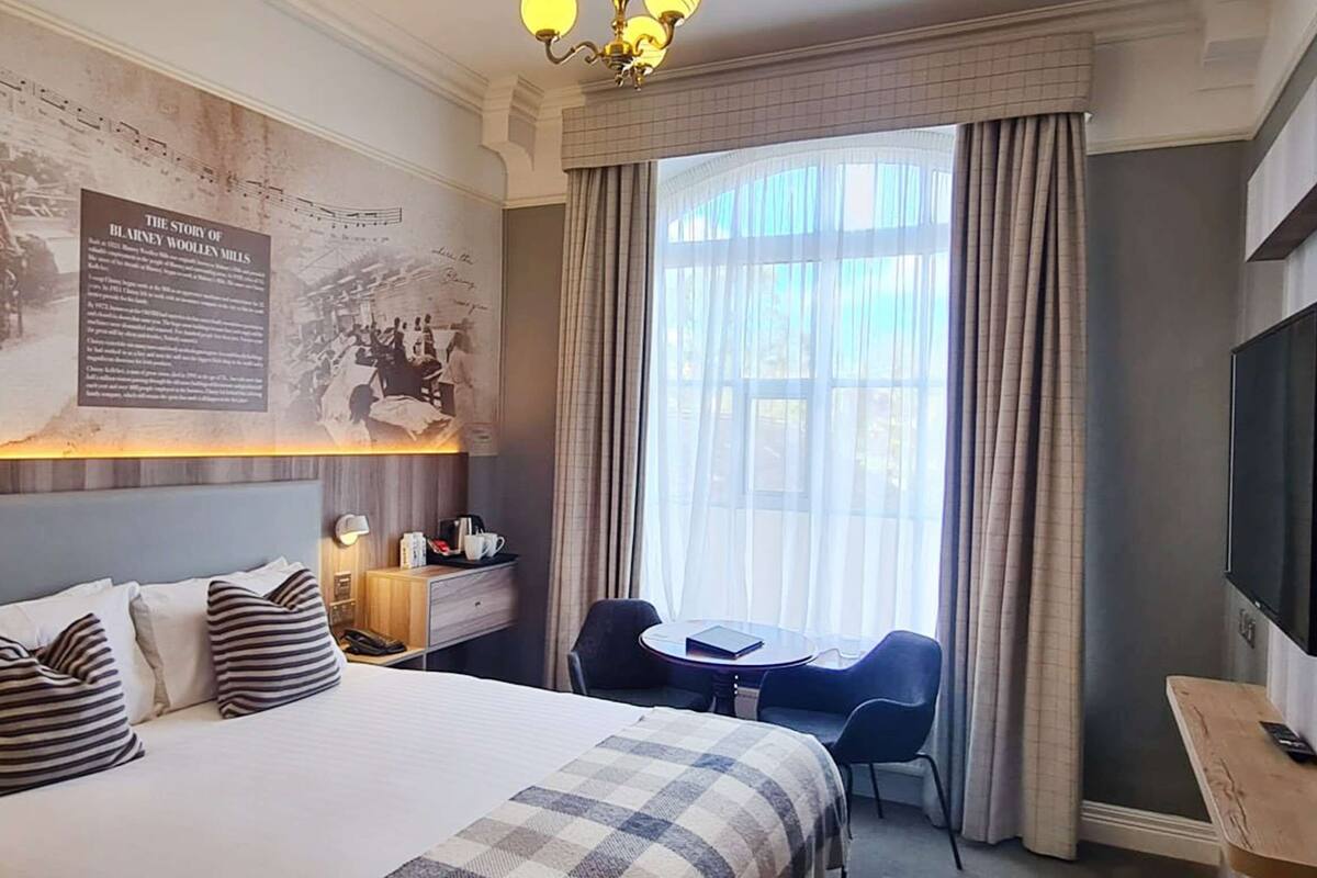 Una habitación de hotel con una cama grande, un escritorio con silla, un televisor y una ventana con cortinas.