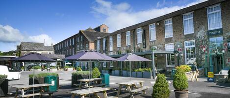 A parking lot with picnic tables and umbrellas, a café, and a restaurant with a signboard.