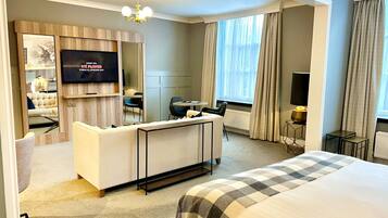 A hotel room with a large bed, a TV mounted on the wall, a seating area with a sofa and chairs, and a small table.