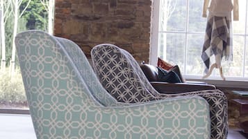 Una habitación con dos sillones estampados, un ventanal con vista a árboles, y un maniquí vestido con suéter y bufanda.
