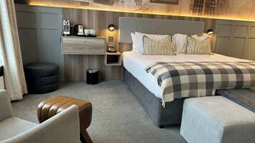 Una habitación de hotel moderna con una cama grande, una mesita de noche de madera, una silla, un pequeño otomaní y un estante montado en la pared.