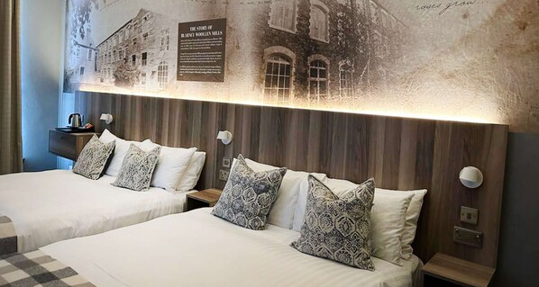 A hotel room with two beds, patterned pillows, a wall-mounted light, and a historical plaque. - Blarney Woollen Mills Hotel, BW Signature Collection (Blarney)