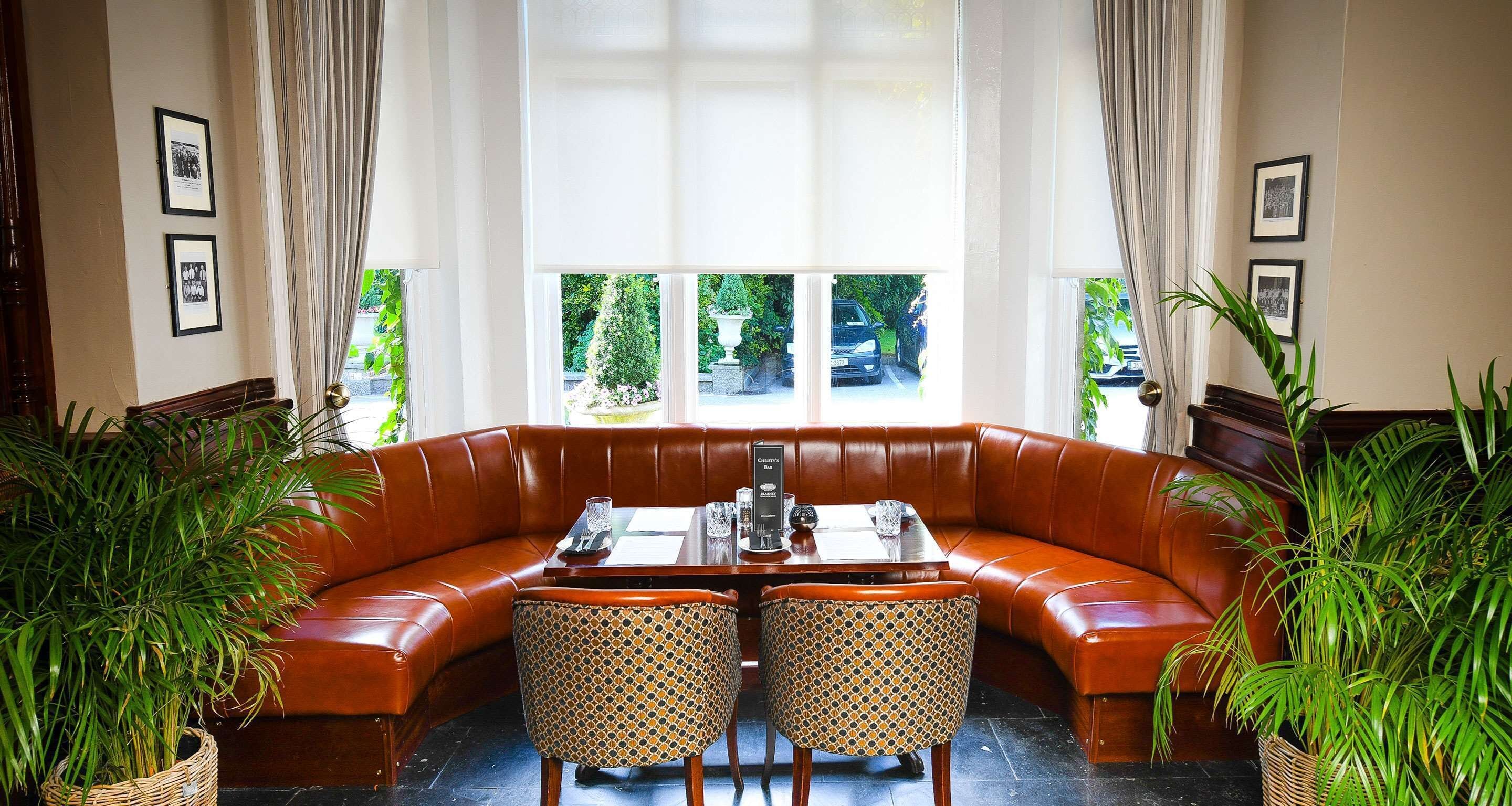 A corner seating area with a brown leather sofa and a dining table with chairs. There are two potted plants on either side of the sofa.