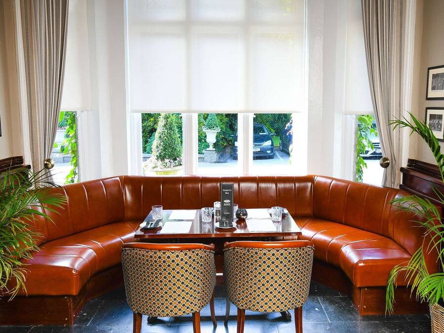 A corner seating area with a brown leather sofa and a dining table with chairs. There are two potted plants on either side of the sofa.