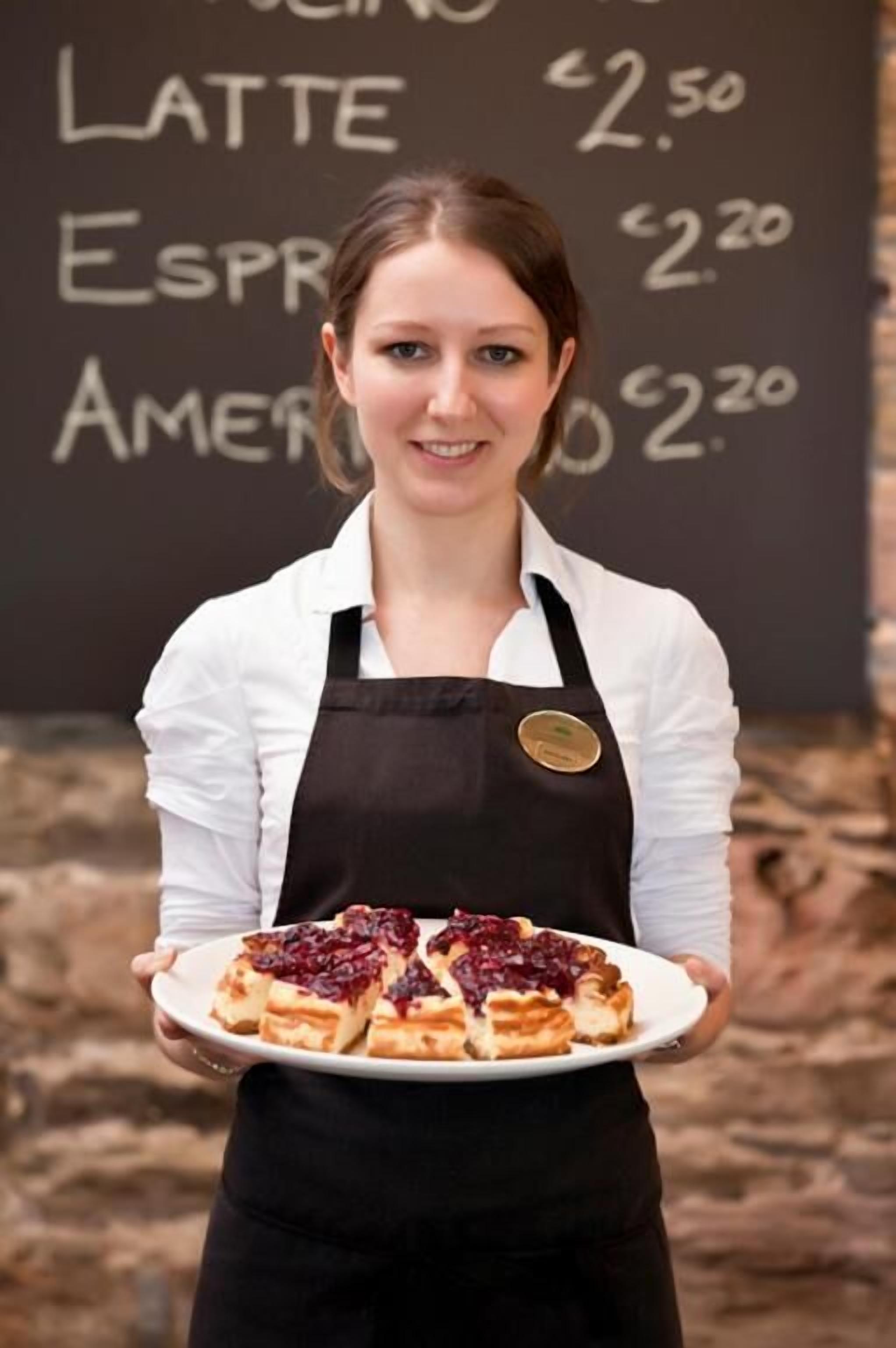 Una persona che tiene un piatto di cibo, con un menu scritto su una lavagna sullo sfondo.
