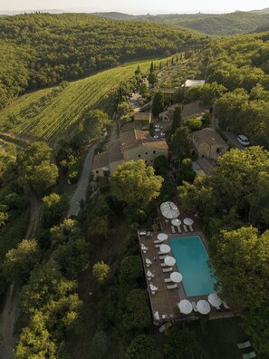 An aerial view of a villa surrounded by vineyards, with a swimming pool and outdoor seating area. - Borgo Vescine (Radda in Chianti)