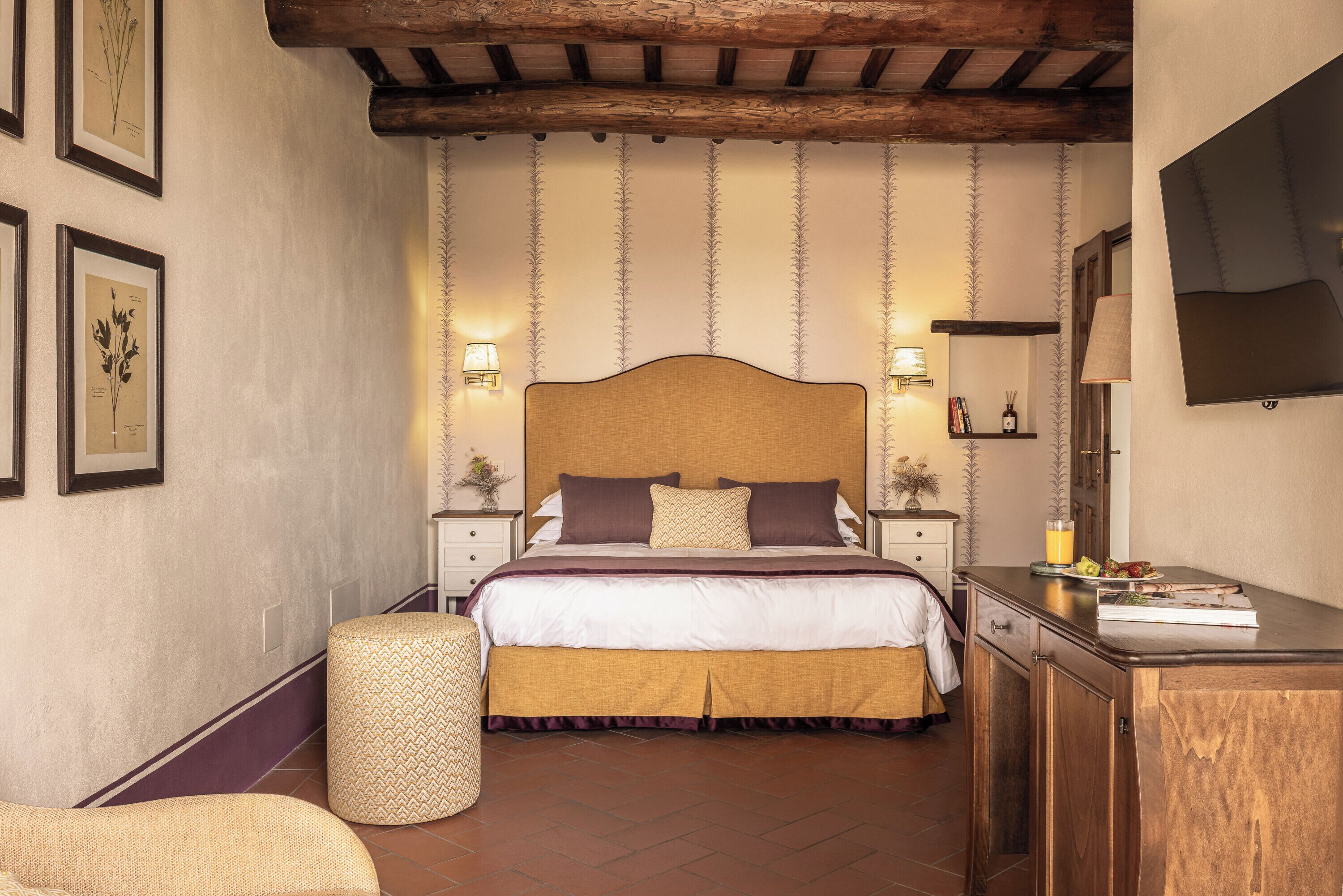 Un dormitorio con una cama grande, lámparas de noche, cabecera de madera, una mesita de noche con libros y un televisor montado en la pared.