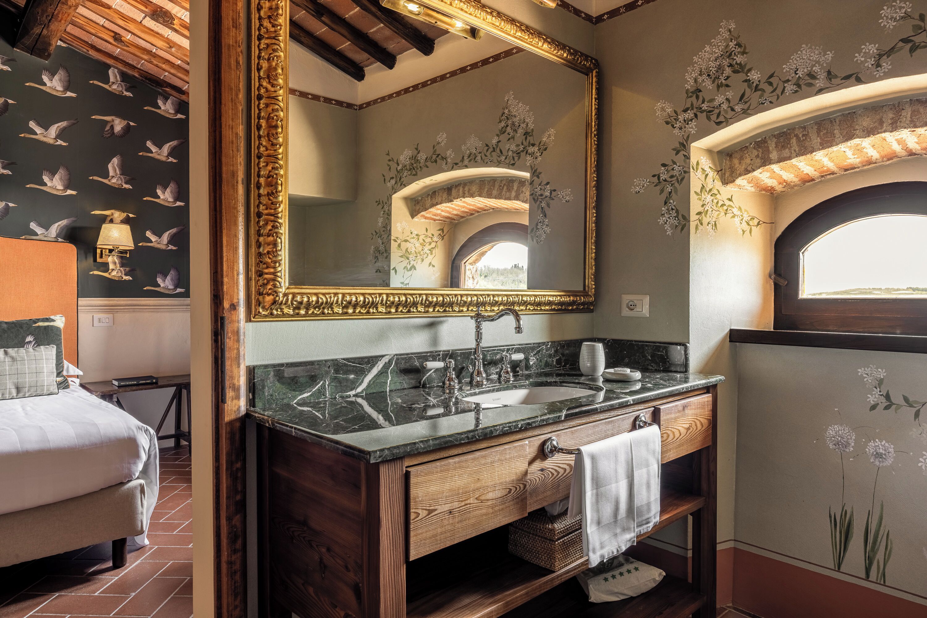 A bathroom with a large mirror, marble countertop, wooden vanity, and floral wall decor.