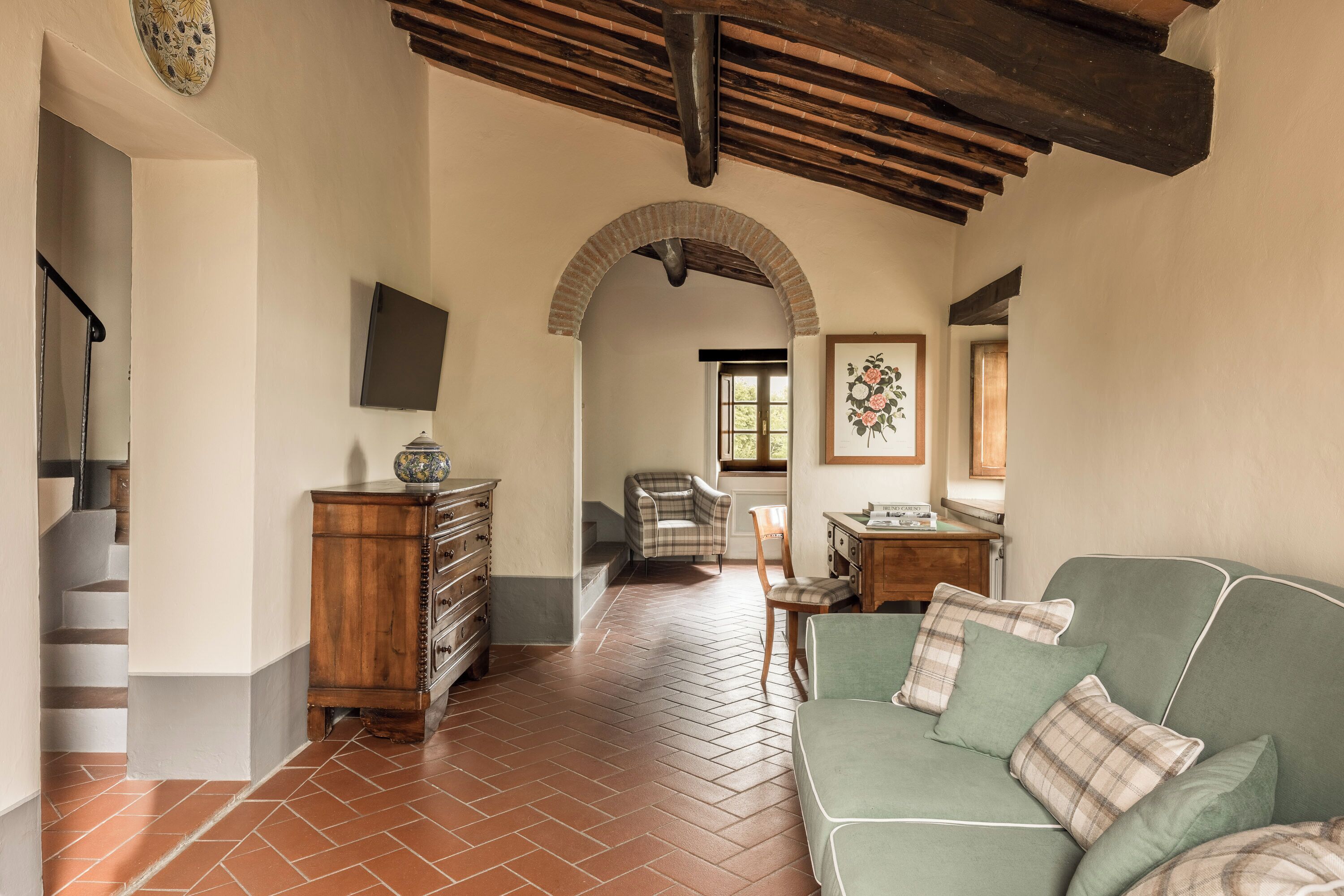 Un espacio habitable amplio con piso de espiga, un sofá verde con cojines escoceses, un mueble de madera y una silla.