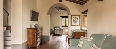 Un espacio habitable amplio con piso de espiga, un sofá verde con cojines escoceses, un mueble de madera y una silla.