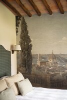 Un dormitorio con cama, almohadas, una lámpara y un mural con un paisaje urbano en la pared.