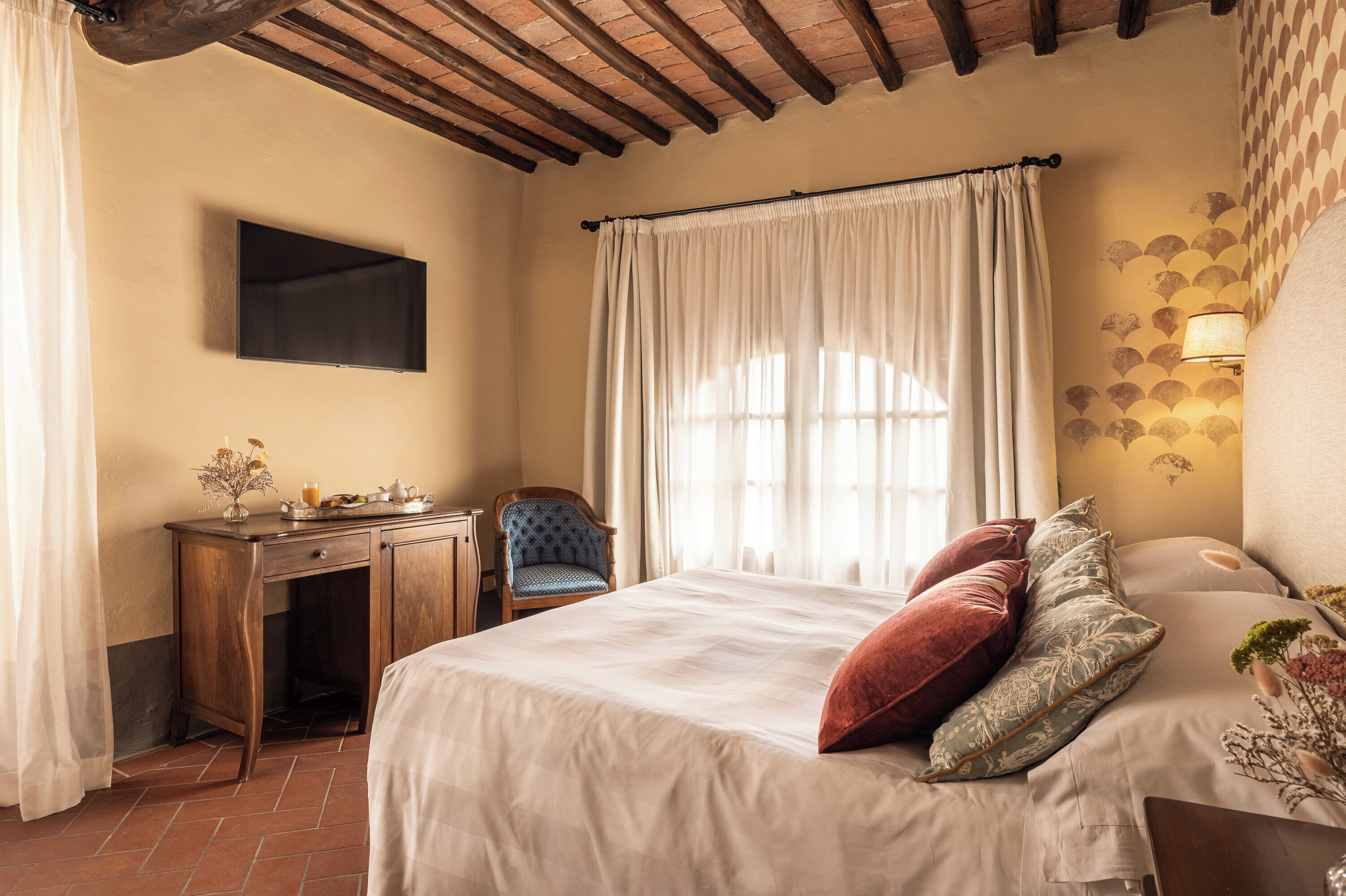 Un dormitorio con cama, escritorio, silla, televisor y ventana con cortinas.
