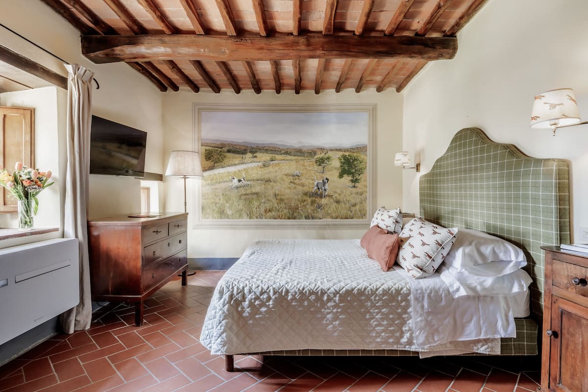 A bedroom with a bed, a dresser, a TV, a painting, and a lamp.