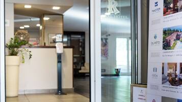 Ein Hotel-Empfangsbereich mit Empfangstresen, einer Zimmerpflanze und einem digitalen Bildschirm.