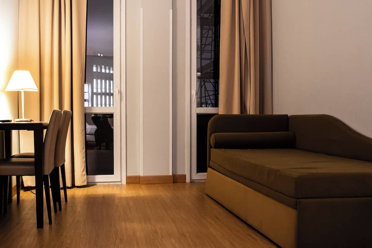 A room with a sofa, a table with chairs, a lamp, and a view through a door.