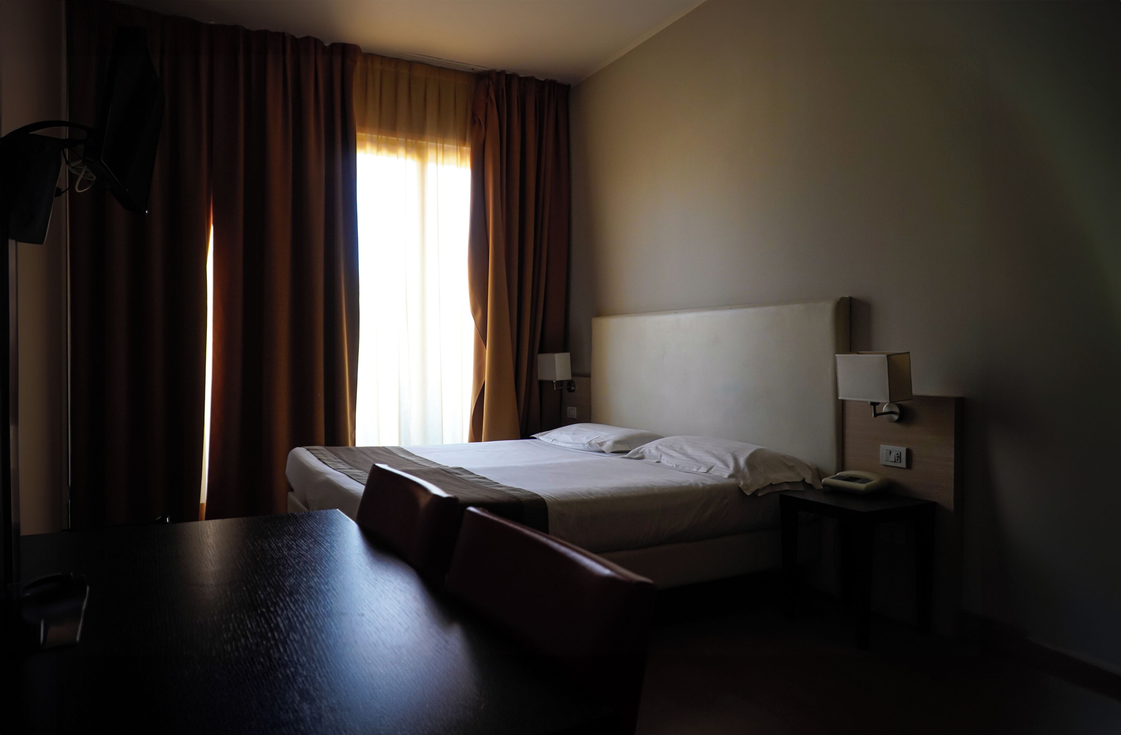 A hotel room with a bed, bedside lamps, a desk, and a chair.
