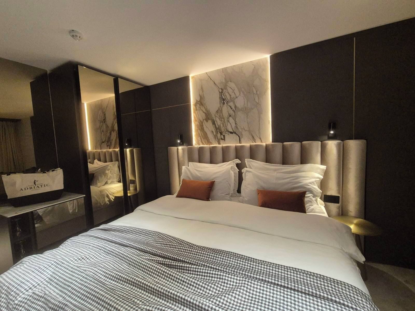 Una habitación de hotel moderna con una cama grande, una pared de mármol y un espejo.