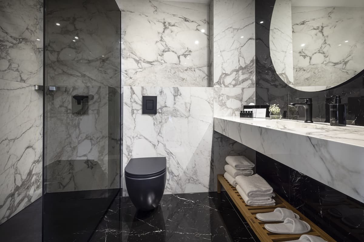 A modern bathroom with a marble wall, a black toilet, a vanity with a mirror, and neatly folded towels.