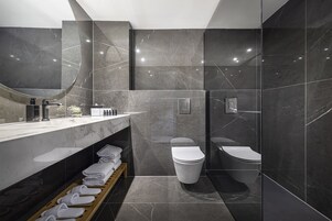 Une salle de bain moderne avec un meuble-lavabo en marbre, deux toilettes et une douche séparée par une paroi de verre.