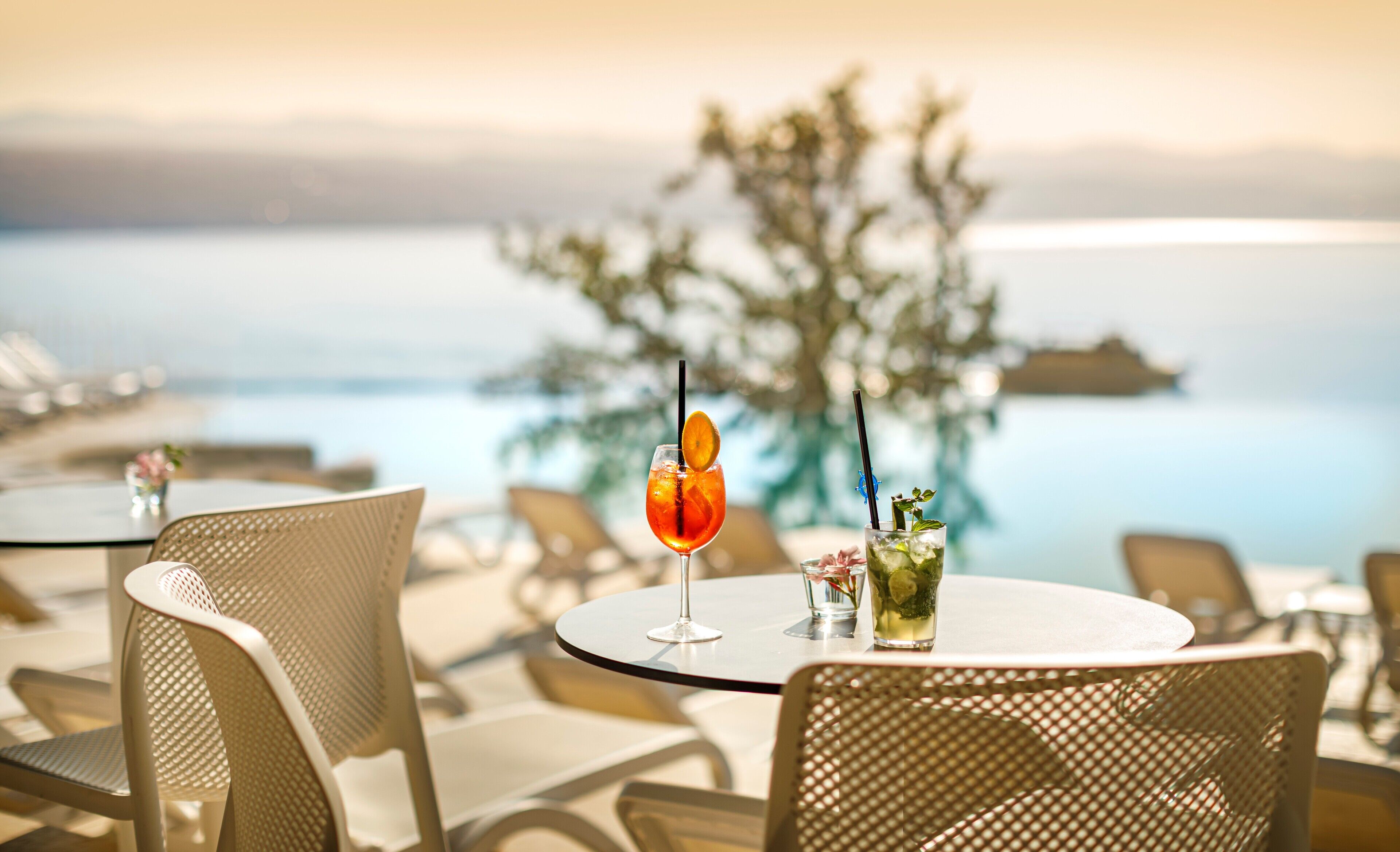 A table with two drinks, a chair, and a view of the sea.