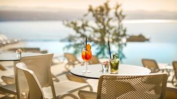 A table with two drinks, a chair, and a view of the sea.