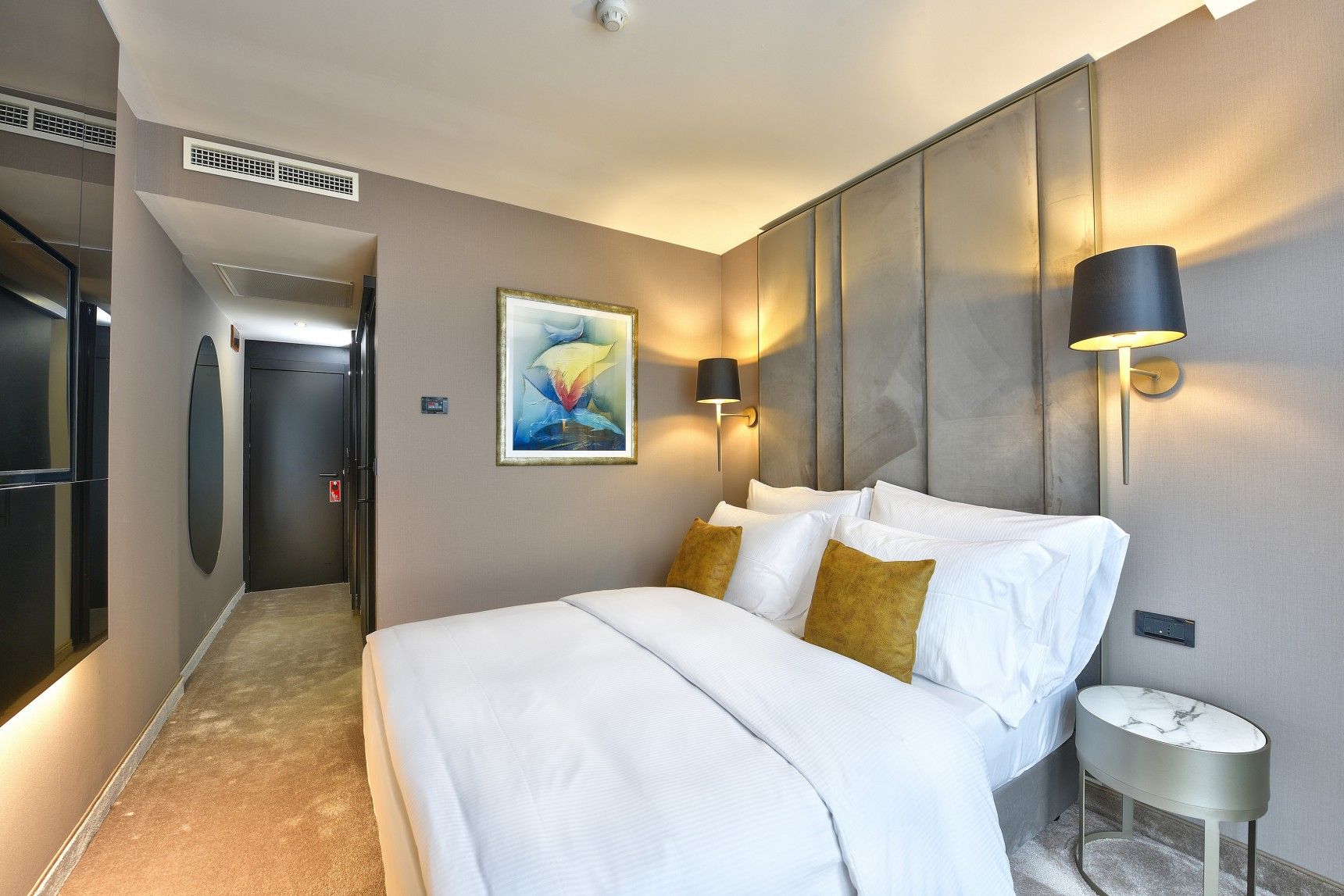 Habitación de hotel con cama, mesita de noche, lámpara de pared y un cuadro.