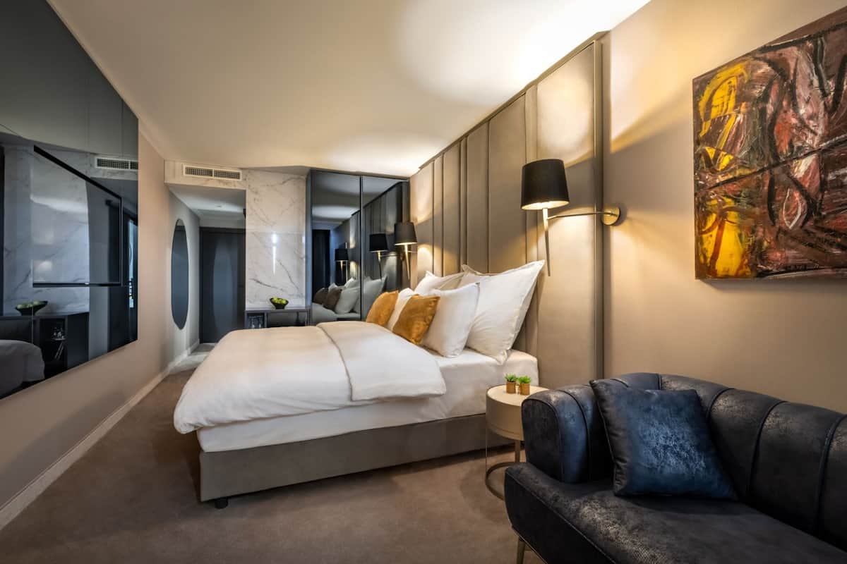A modern hotel room with a large bed, a seating area, and a painting on the wall.