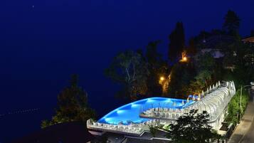 A modern hotel with a large outdoor swimming pool, surrounded by trees and a well-lit pathway.