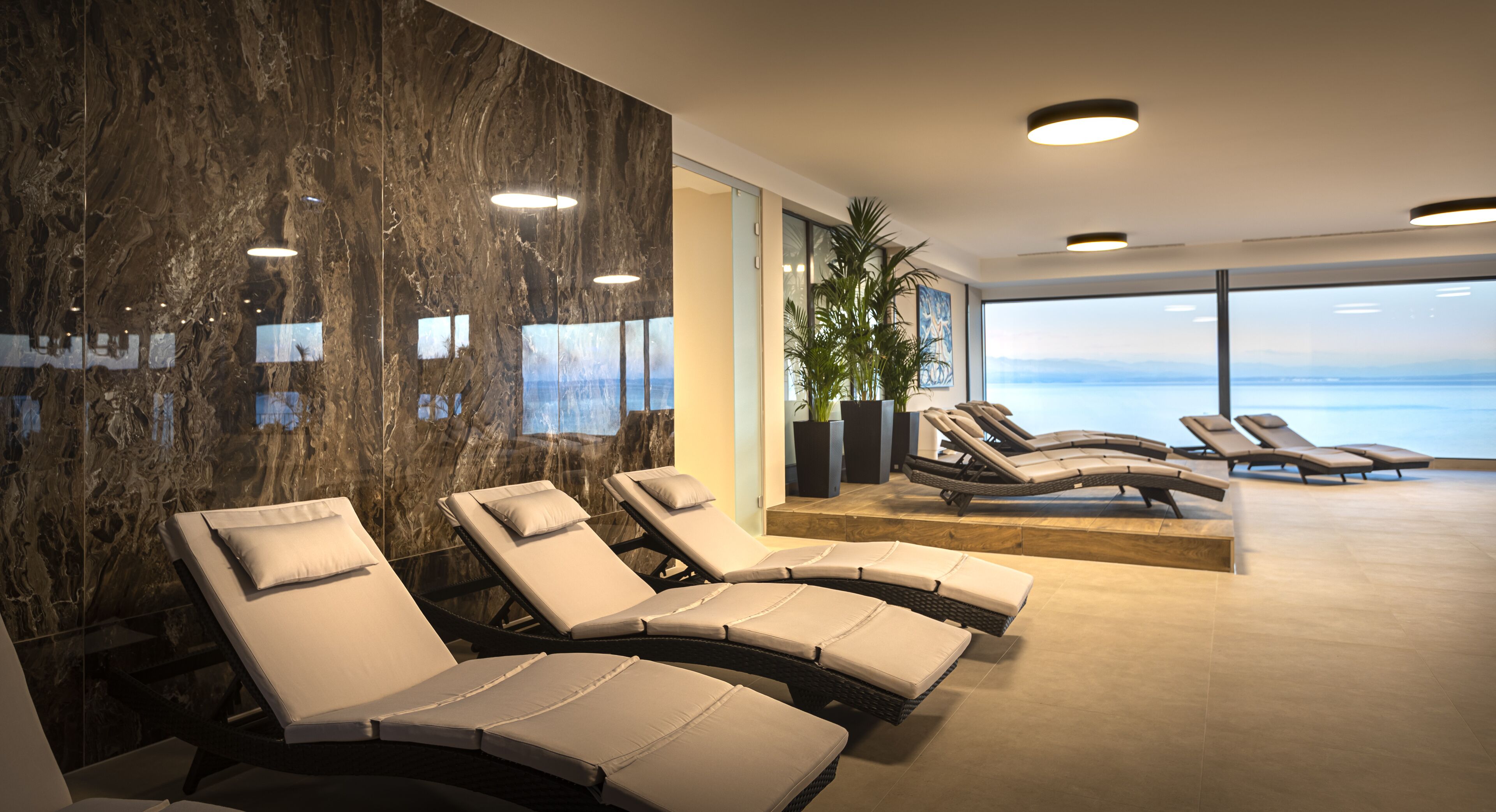 A modern spa area with reclining chairs, a large mirror, and a view of the sea.