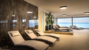 A modern spa area with reclining chairs, a large mirror, and a view of the sea.