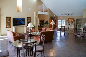 A spacious living area with a glass-top table, multiple chairs, sofas, and a television. - The Oasis (Palm Springs)