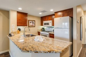A kitchen with granite countertops, wooden cabinets, a stainless steel refrigerator, and a microwave. - The Oasis (Palm Springs)