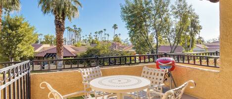 A balcony with a table and chairs, a grill, and a view of palm trees and houses.