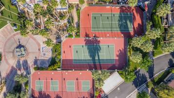 An aerial view of a sports complex with multiple tennis courts, surrounded by greenery and a parking area.