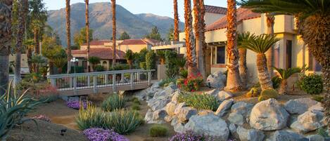 A resort with palm trees, a bridge, and a mountainous backdrop.