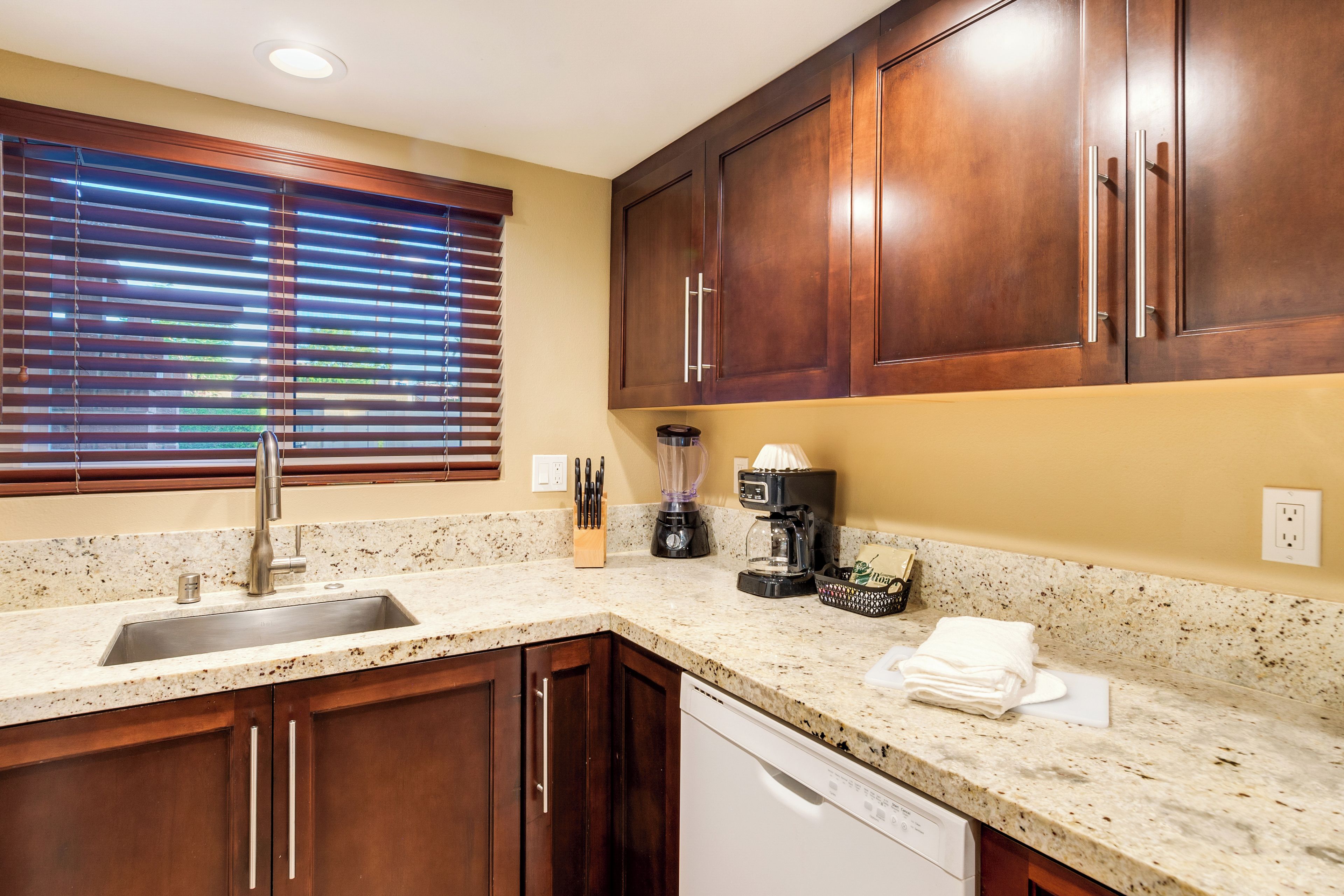 A kitchen with wooden cabinets, a granite countertop, a sink, a coffee maker, and a dishwasher.