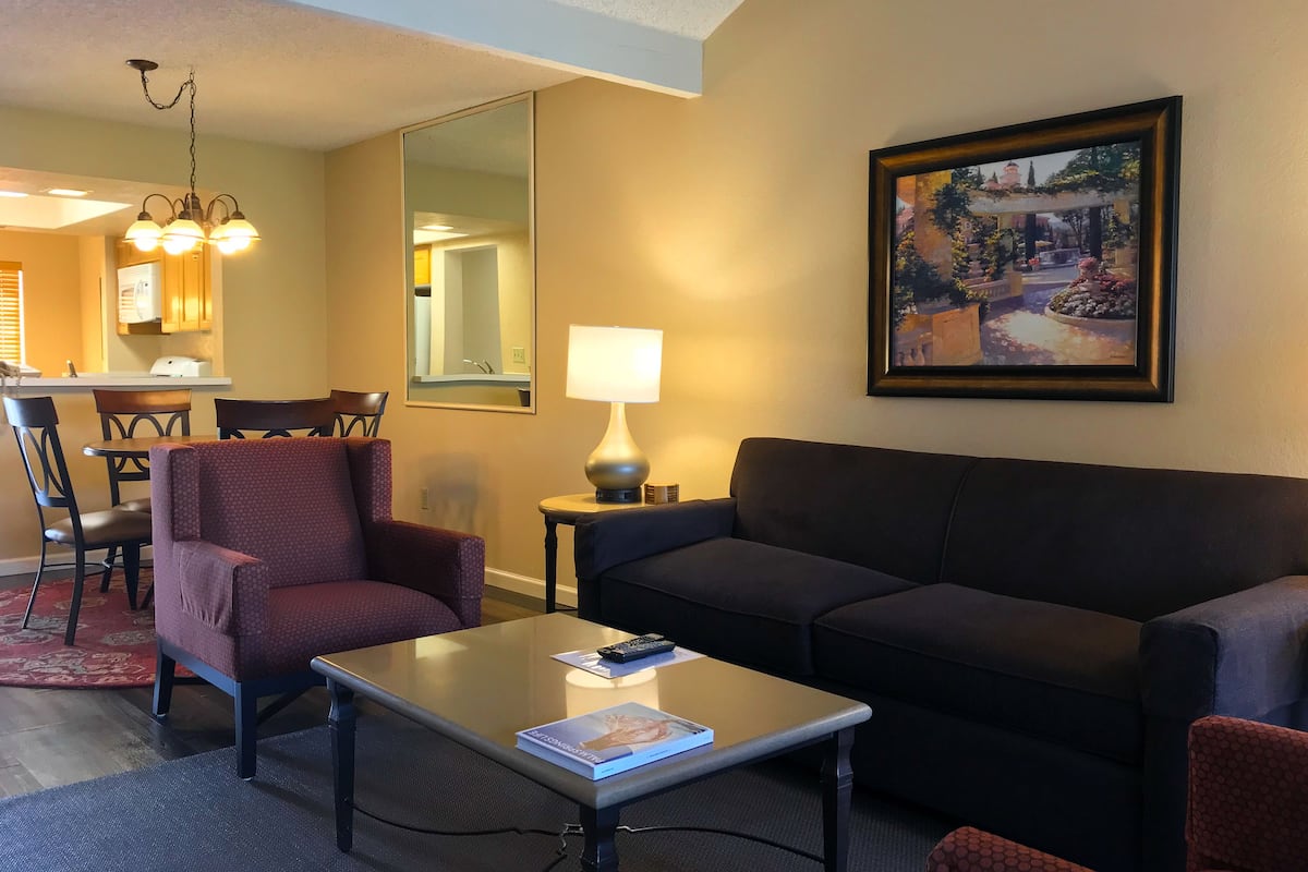 A living room with a sofa, armchair, coffee table, and a painting on the wall.