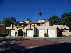 A residential building with a red-tiled roof, multiple garage doors, and a landscaped driveway.