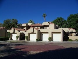 A residential building with a red-tiled roof, multiple garage doors, and a landscaped driveway.