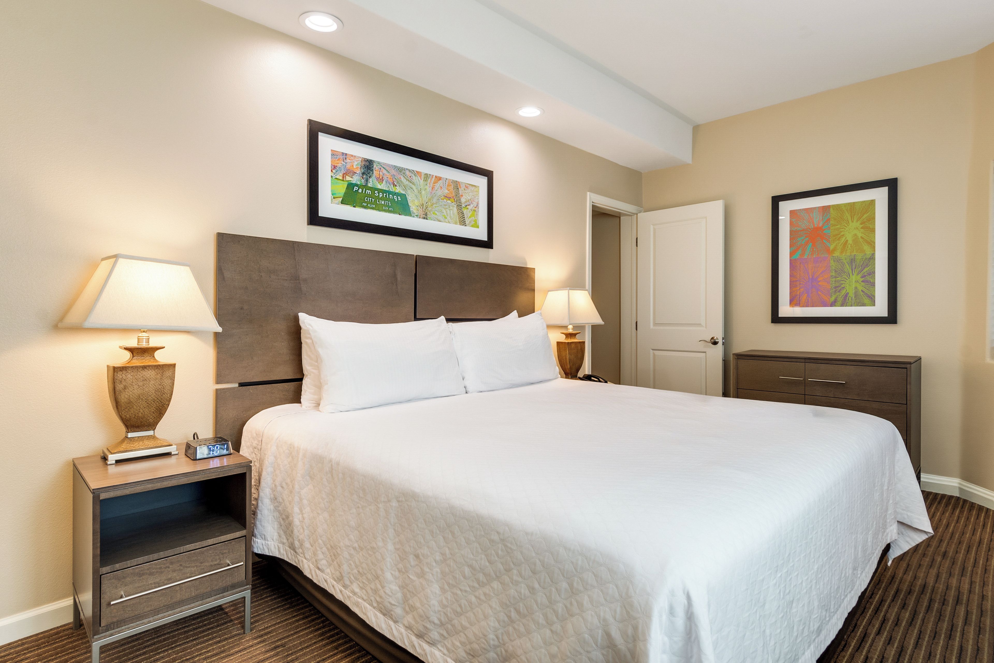 A hotel room with a large bed, two bedside tables, a nightstand, a wardrobe, and two wall-mounted lamps.