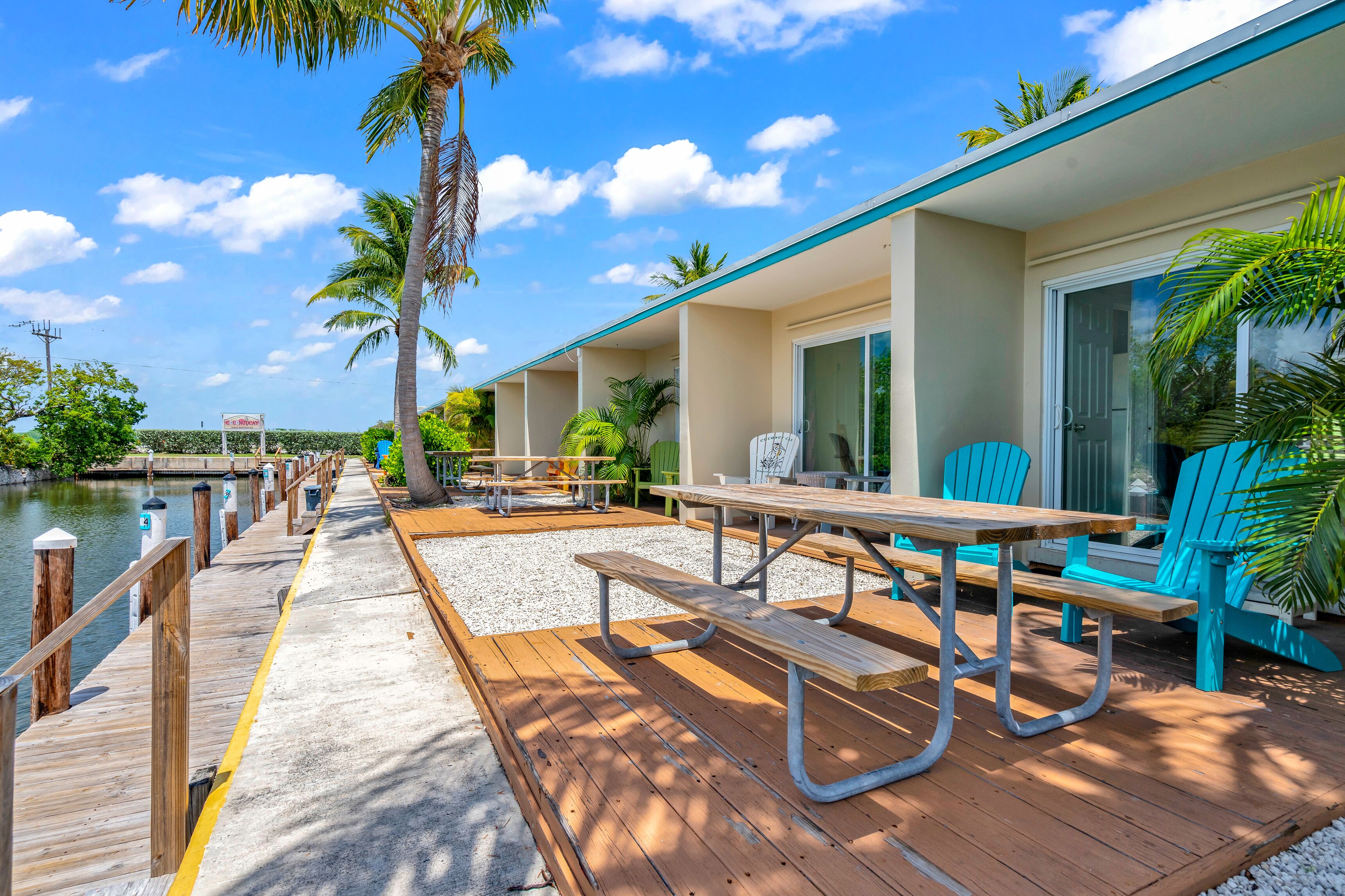 A wooden deck with picnic tables and chairs, a dock extending into a body of water, and a building with a covered patio area.