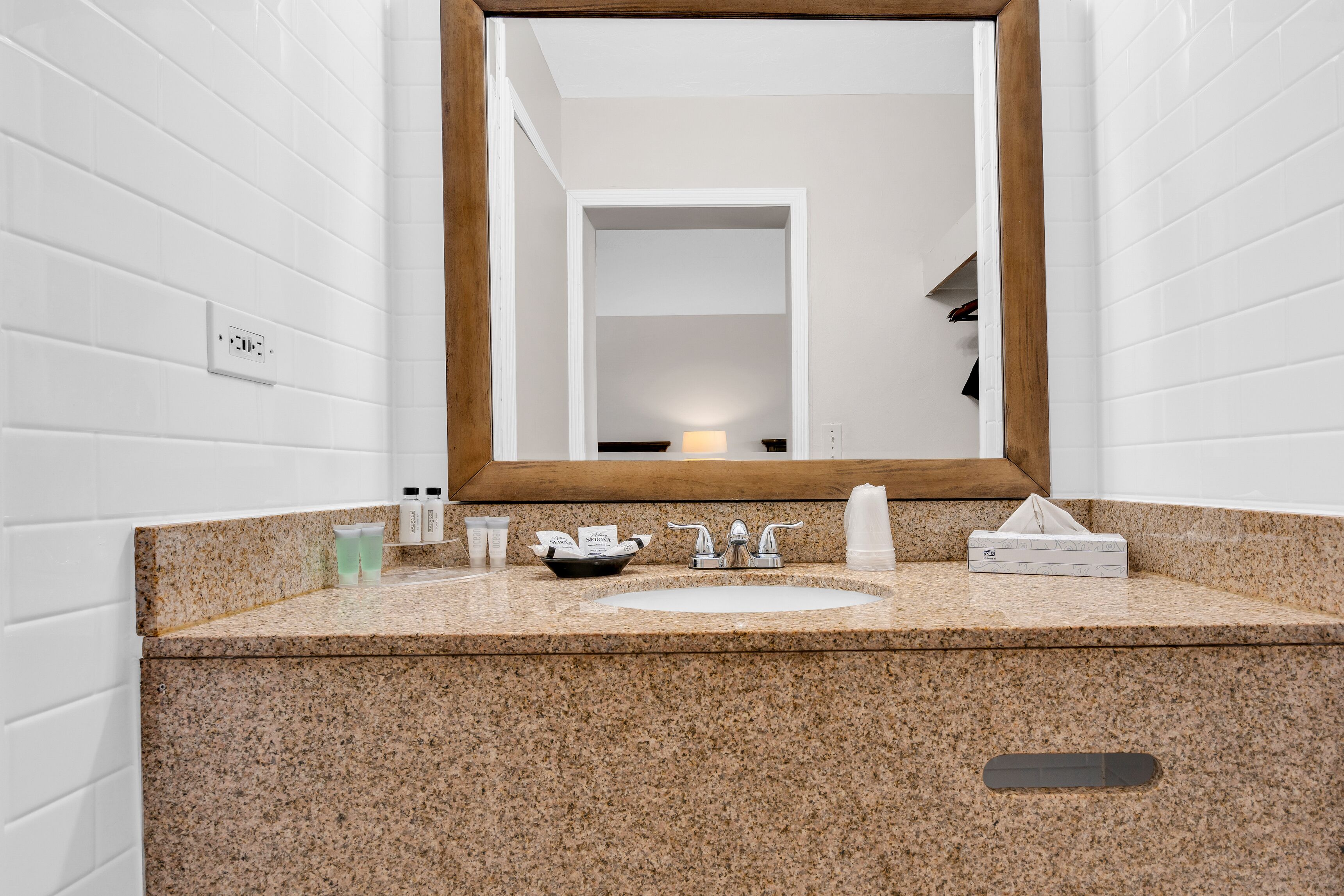 A bathroom with a granite countertop, a sink, a mirror, and toiletries.
