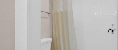 A bathroom with white tiled walls, a toilet, and a shower with a transparent curtain.