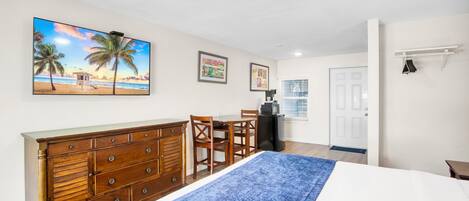 Une chambre à coucher avec un lit, une commode, un bureau et des chaises. Un tableau représentant une scène de plage est accroché au mur.
