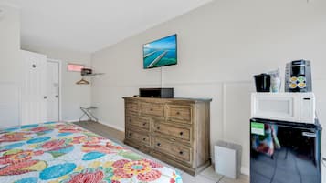 Um quarto com cama, cômoda, televisão, micro-ondas e geladeira.
