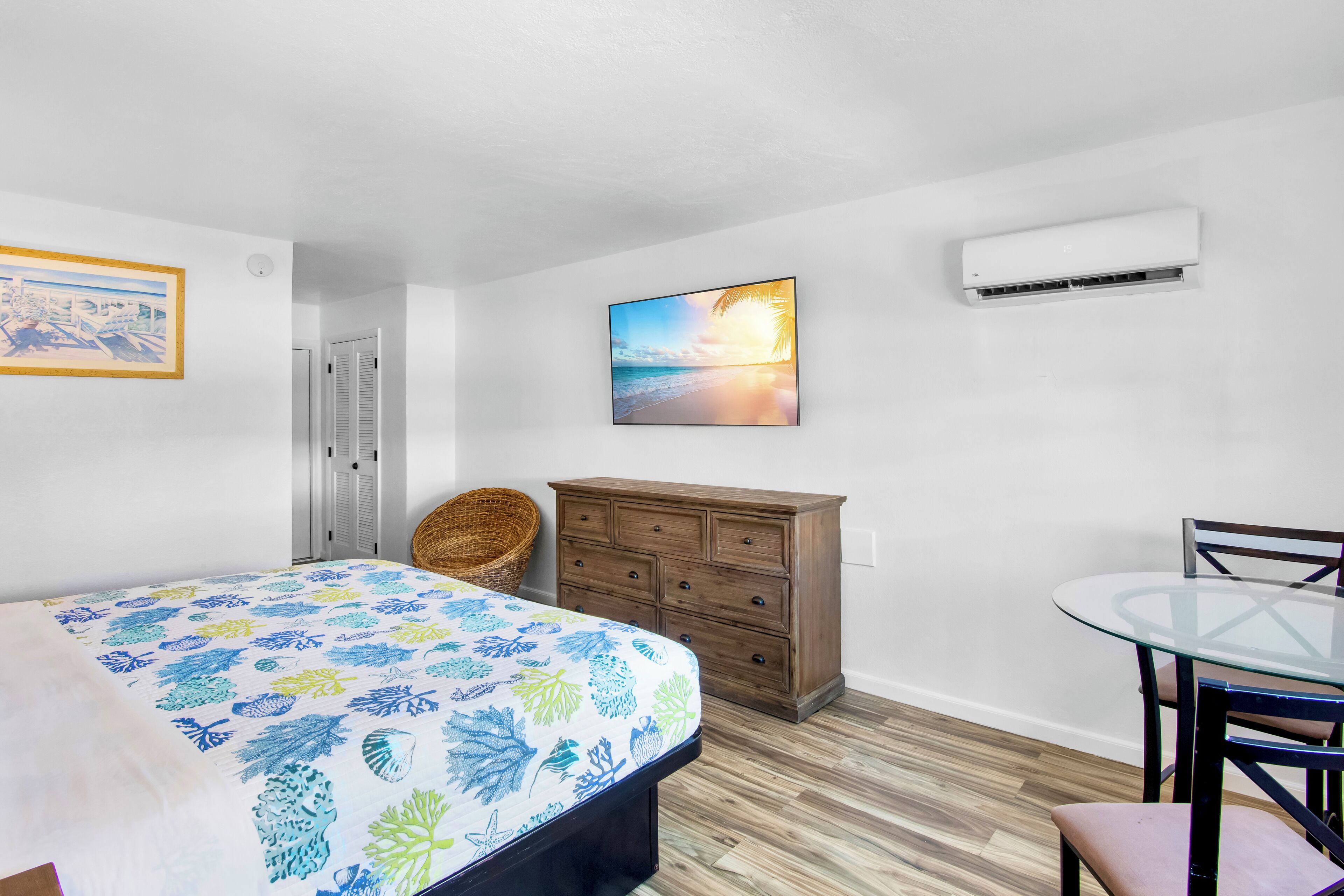 Un dormitorio con cama, cómoda, silla, mesa y aire acondicionado.